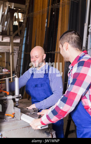 Two positive workmen in uniform working on machine in PVC shop Stock Photo