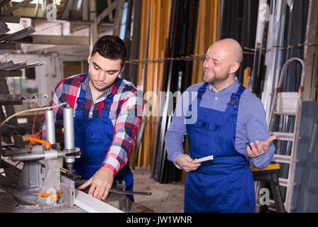 Two workmen in uniform working on machine in PVC shop indoor Stock Photo