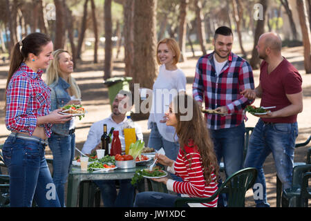 Happy smiling friends making grill at summer corporate party outdoors. Selective focus Stock Photo