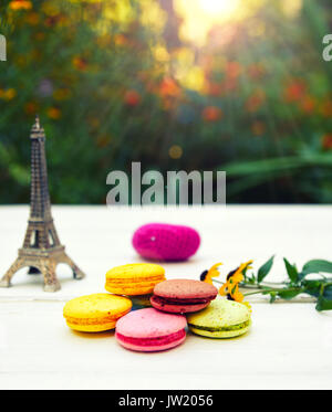 Colored cakes macarons  on a white table, behind a bright sun shines through green bushes Stock Photo