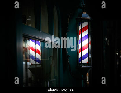 Barber shop pole by the entrance lights up in the dark. Stock Photo