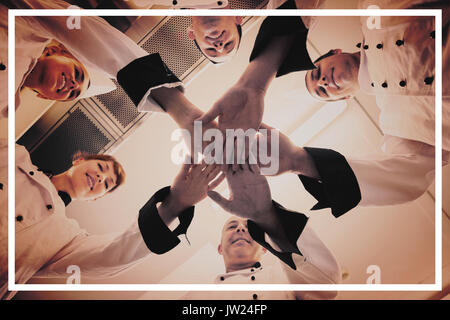 Chefs joining hands in a circle wearing uniforms in a kitchen Stock Photo