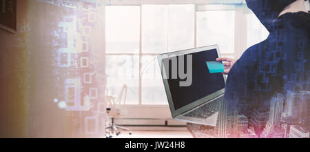 Rear view of hacker using laptop and credit card against composite image of shiny spiral of binary code Stock Photo