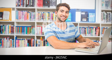 Student on laptop against various books on shelf in library Stock Photo