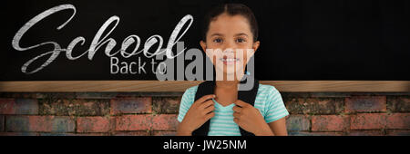 Portrait of smiling girl with bag against blackboard on brick wall Stock Photo