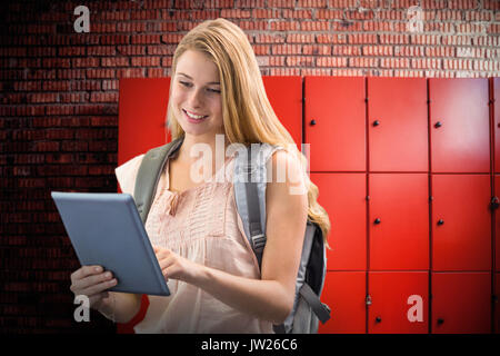 Happy student using tablet against orange lockers against brick wall Stock Photo