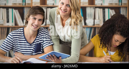 Teacher helping student in class against various multi colored books on shelf Stock Photo