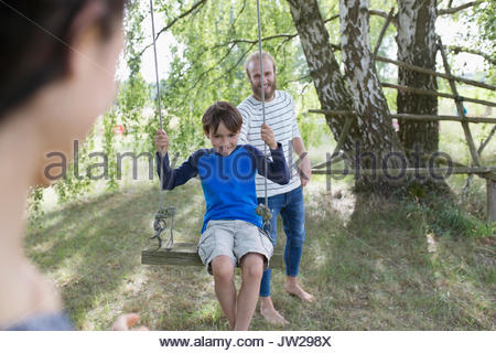 Father pushing son on tree swing in rural yard