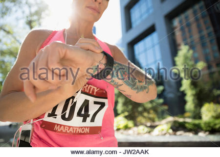 Tattooed female marathon runner checking smart watch in urban park