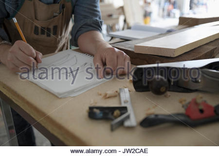 Close up male carpenter sketching in notebook at workbench