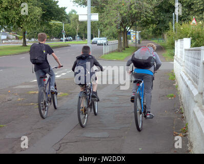 three boys on bicycles ride on the sidewalk enjoying summer holidays or travelling to school with bags Stock Photo
