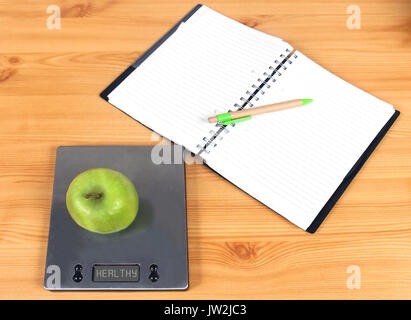 Open blank pages notebook with green apple on kitchen scale representing health diet lifestyle concept Stock Photo