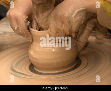 Beginner and teacher in process of making clay bowl on pottery wheel. Potters at work. Stock Photo