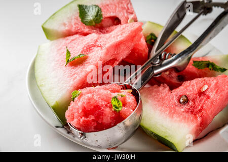 Summer fruit desserts, frozen cocktails. Ice cream granite from watermelon with mint, one scoop in spoon for ice cream, on plate with slices of waterm Stock Photo