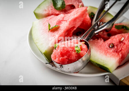 Summer fruit desserts, frozen cocktails. Ice cream granite from watermelon with mint, one scoop in spoon for ice cream, on plate with slices of waterm Stock Photo