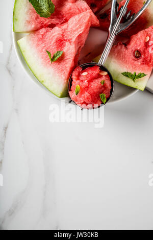 Summer fruit desserts, frozen cocktails. Ice cream granite from watermelon with mint, one scoop in spoon for ice cream, on plate with slices of waterm Stock Photo