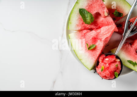 Summer fruit desserts, frozen cocktails. Ice cream granite from watermelon with mint, one scoop in spoon for ice cream, on plate with slices of waterm Stock Photo