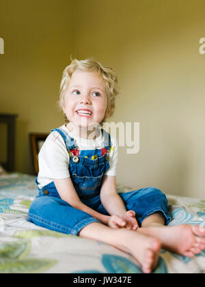 Smiling boy (4-5) sitting on bed and looking away Stock Photo