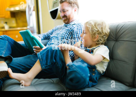 Boy (4-5) and man using digital tablet on sofa in living room Stock Photo