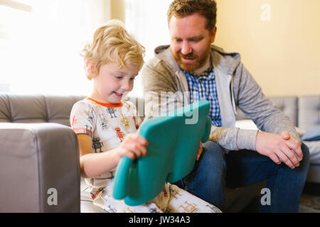 Boy (4-5) and man using digital tablet on sofa in living room Stock Photo