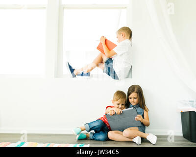 Boy (6-7) reading book and sister with brother (2-3, 6-7) using digital tablet Stock Photo