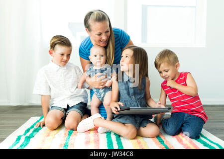 Mother with children (6-11 months, 2-3, 6-7) using digital tablet at home Stock Photo