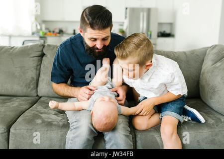 Father and boy (6-7) playing with baby boy (6-11 months) in living room Stock Photo