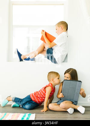 Boy (6-7) reading book and sister with brother (2-3, 6-7) using digital tablet Stock Photo