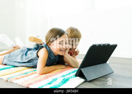 Siblings (2-3, 6-7) lying down on carpet and watching digital tablet Stock Photo
