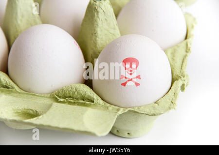 Eggs in paper package with one egg painted with a red poisonous risk symbol skull and bones. Image concept for food contamination and egg scandal. Stock Photo