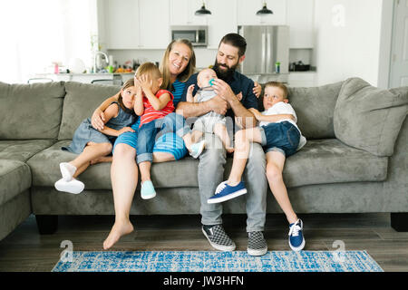 Family with four children (6-11 months, 2-3, 6-7) spending time on sofa Stock Photo