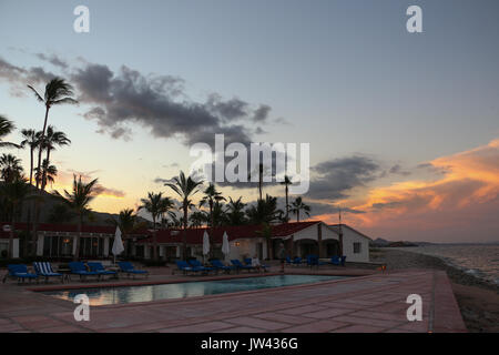 View of Rancho Las Cruces Resort after the sun has just set, illuminating the clouds. The hotel is on the Sea of Cortez, palms and pool beckon. Stock Photo