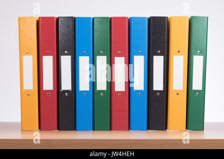 A row of multicoloured office document folders on a timber book shelf with plain white background and copy space. Stock Photo