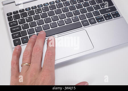 Close up of a mans hand on the mouse tracking pad of a laptop computer keyboard with white copy space. Stock Photo