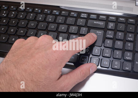Close up of a mans finger pressing the enter button on a computer laptop keyboard. Stock Photo