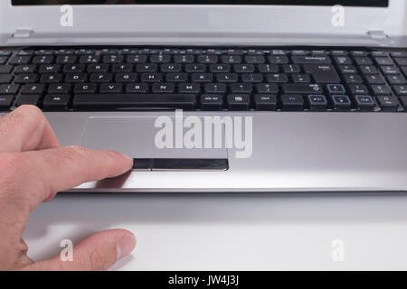 A close up of a mans finger left clicking the mouse pad button on a computer laptop keyboard. Stock Photo