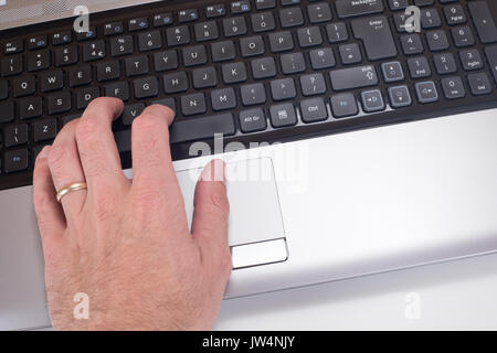 A close up of a mans hand with a wedding ring typing on a laptop computer keyboard. Stock Photo
