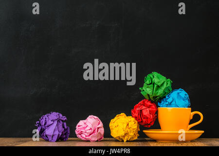 orange coffee cup set filled with colored junk paper balls place on blackboard background with vintage wood flooring show design inspiration area. Stock Photo