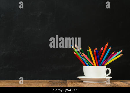 back to school learning concept with white coffee cup group put lots of rainbow pencils show in classroom blackboard wall background on wood desk. Stock Photo