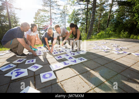Full length of male and female business people solving crossword on patio in forest Stock Photo