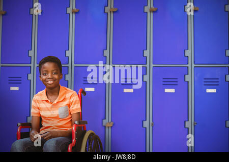 Full length portrait of happy boy on wheelchair against purple closed lockers in school Stock Photo