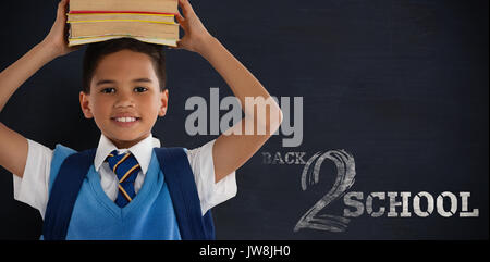 Smiling schoolboy carrying books on head over white background against black background Stock Photo
