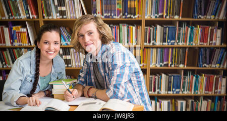 College students doing homework in library against various books on shelf Stock Photo