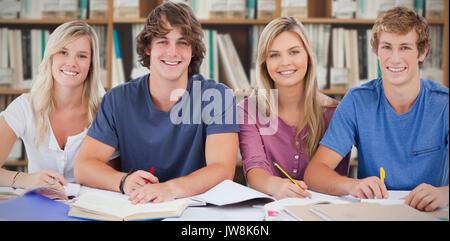 Four students looking at the camera against various multi colored books on shelf Stock Photo
