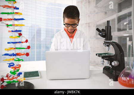 Schoolboy using laptop at desk against modern room overlooking city Stock Photo