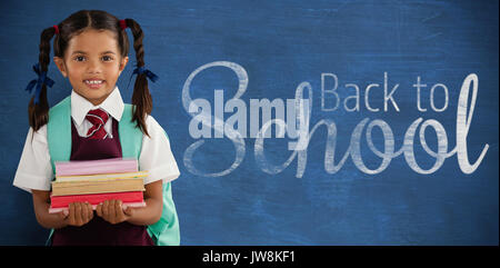 Smiling schoolgirl carrying books against blue background Stock Photo