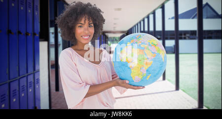 Smiling woman holding globe against empty corridor at school Stock Photo