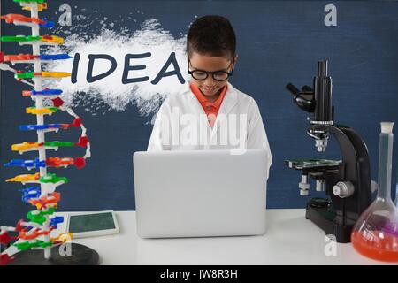 Digital composite of Student boy at table using a computer against blue blackboard with idea text Stock Photo