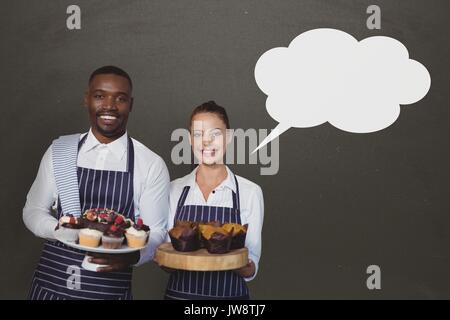 Digital composite of Small business owners couple with speech bubble holding cupcakes against grey background Stock Photo