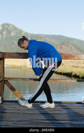 Side view of female athlete exercising on pier against clear sky Stock Photo